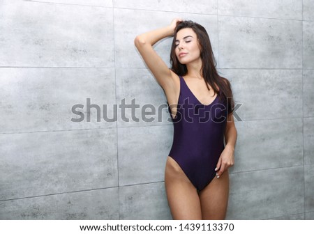 Beautiful young woman in bikini near tiled wall at shower room, space for text. Spa treatment