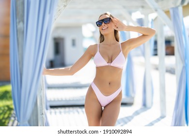 Beautiful young woman in bikini swimsuit posing at chaise lounge near swimming pool