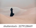 Beautiful young woman with a black abaya walking on the dunes in the desert.