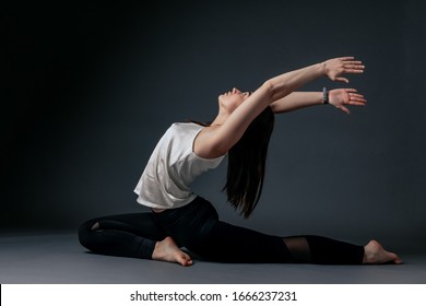 Beautiful young woman in black sweatpants and white top practicing yoga, standing in a pose of a warrior, doing Virabhadrasana exercise, attractive girl working modern yoga studio gray background home - Shutterstock ID 1666237231