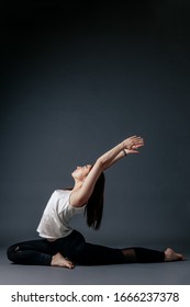 Beautiful young woman in black sweatpants and white top practicing yoga, standing in a pose of warrior, doing Virabhadrasana exercise, attractive girl working a modern yoga studio gray background home - Shutterstock ID 1666237378