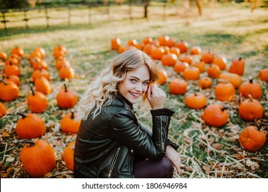 Schöne junge Frau mit blondem Haar in Lederjacke sitzend auf einem Kürbisfeld und Lächeln. Herbsthintergrund. . Hochwertiges Foto