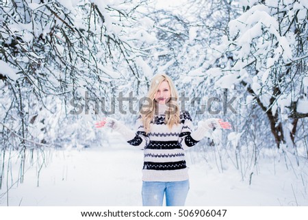 Beautiful young woman with blond hair is dressed in a warm black and white sweater on the snowy background in the winter forest. / Beautiful young woman throwing snow and smiling. Christmas theme