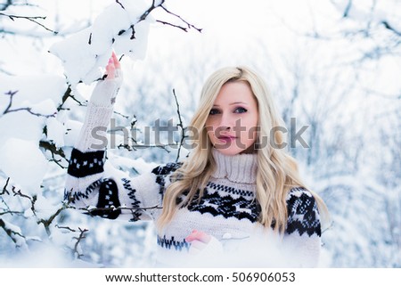Beautiful young woman with blond hair dressed in a warm black and white sweater, holds a snowy tree branch. Snowy winter forest, Christmas theme