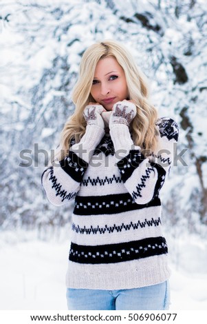 Beautiful young woman with blond hair is dressed in a warm black and white sweater. Snowy winter forest, christmas theme
