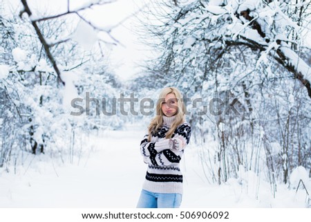 Beautiful young woman with blond hair is dressed in a warm black and white sweater. Snowy winter forest, christmas theme