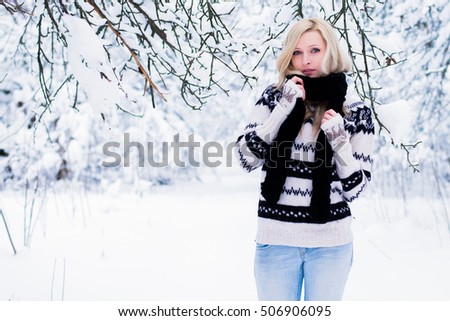Beautiful young woman with blond hair is dressed in a warm black and white sweater and wrapped in a long black scarf. Snowy winter forest, christmas theme