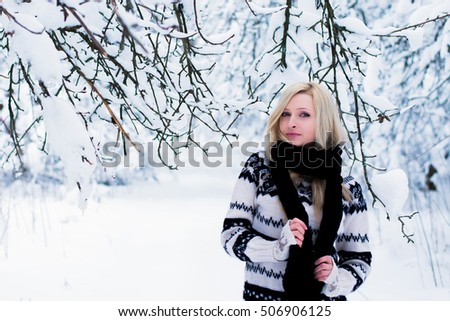 Beautiful young woman with blond hair is dressed in a warm black and white sweater and wrapped in a long black scarf. Snowy winter forest, christmas theme