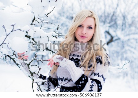 Beautiful young woman with blond hair dressed in a warm black and white sweater, holds a snowy tree branch. Snowy winter forest, Christmas theme