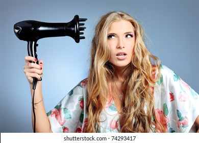 Beautiful Young Woman Is Blowing Dry Her Hair. Studio Shot Over Grey Background.