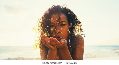 Beautiful young woman blowing glitter on the beach at sunset