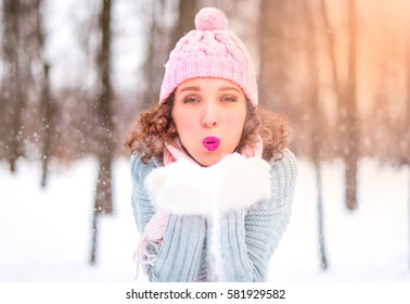 Beautiful young woman is blowing snow from her hands. Magic snowfall effect