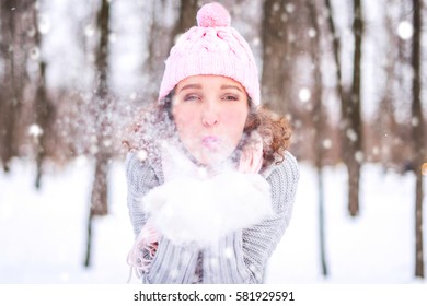 Beautiful young woman blowing snowflakes. Winter young woman portrait. Beauty Joyful Model Girl having fun in winter park. 