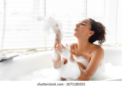 Beautiful young woman blowing soap bubbles and having fun in bath at home, copy space. Charming millennial female relaxing in bathtub with foam, enjoying beauty and skincare day