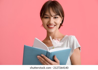 Beautiful young woman with book and flower on pink background