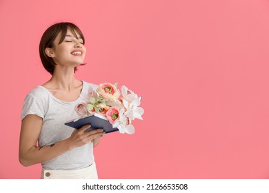 Beautiful young woman with book and flowers on pink background