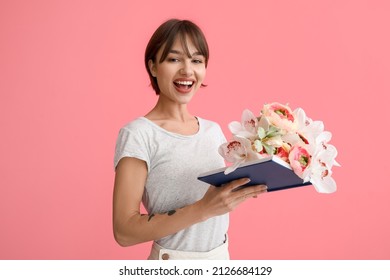 Beautiful young woman with book and flowers on pink background