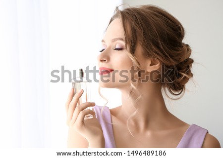 Beautiful young woman with bottle of perfume indoors