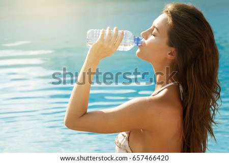Beautiful young woman with a bottle of water beside a swimming pool
