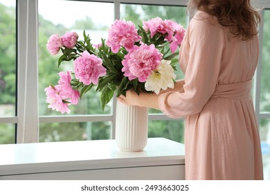 Beautiful young woman with bouquet of peony flowers in vase at home - Powered by Shutterstock