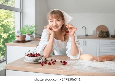 Beautiful young woman with bowl of cherries, rolling pin and dough on table in kitchen - Powered by Shutterstock