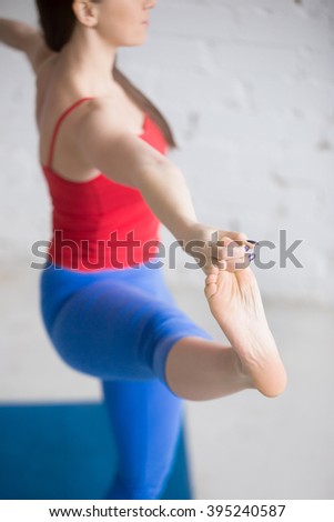 Beautiful young woman in bright colorful sportswear working out indoors in loft interior. Girl standing in Utthita Hasta Padangustasana, Extended Hand to Big Toe Posture. Close-up. Focus on foot