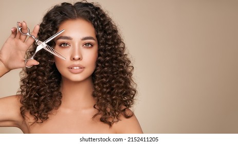 Beautiful Young Woman With A Bright Makeup And A Afro  Hair Holds Metal Scissors. Model With Curly Hair. Hair Salon, Haircut. Care And Beauty Hair Products. Perfect Make-up