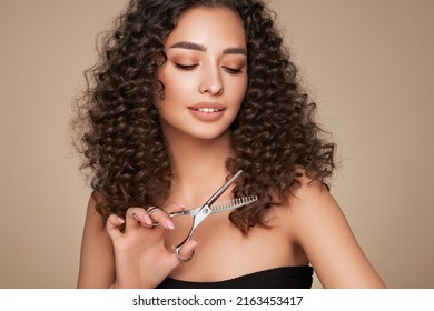 Beautiful Young Woman With A Bright Makeup And A Afro  Hair Holds Metal Scissors. Model With Curly Hair. Hair Salon, Haircut. Care And Beauty Hair Products. Perfect Make-up