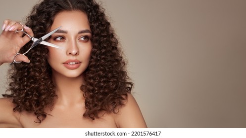 Beautiful Young Woman With A Bright Makeup And A Afro  Hair Holds Metal Scissors. Model With Curly Hair. Hair Salon, Haircut. Care And Beauty Hair Products. Perfect Make-up