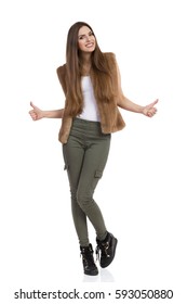 Beautiful Young Woman In Brown Fur Waistcoat, Khaki Pants And Black Boots Standing And Showing Thumbs Up. Full Length Studio Shot Isolated On White.