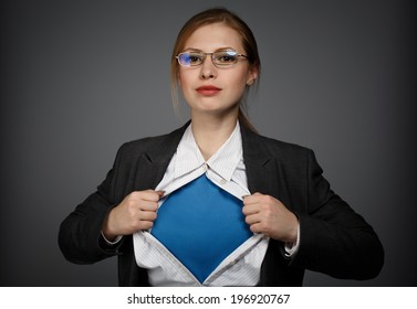 Beautiful Young Woman In Business Suit And Glasses With Superman Concept On Grey Background