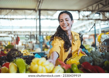 Beautiful young woman buying vegetables. Young cheerful woman at the market. Raw food, veggie concept. Portrait of smiling good looking girl in casual clothing
