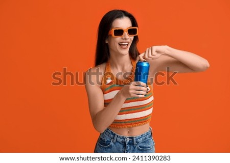 Beautiful young woman with can of cold beer on orange background