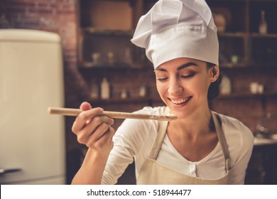 Beautiful young woman in chef hat is holding wooden spoon and smiling