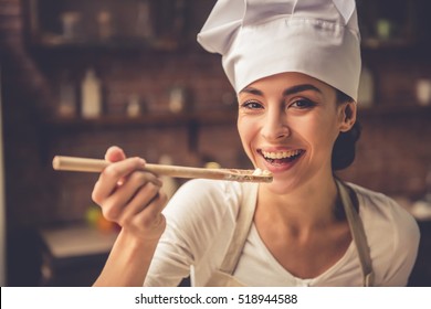 Beautiful young woman in chef hat is holding wooden spoon, looking at camera and smiling
