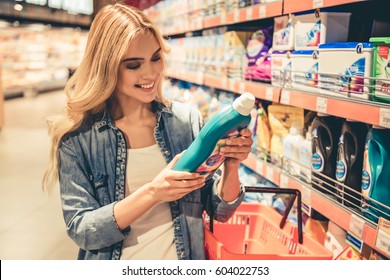 Beautiful Young Woman Is Choosing Household Products And Smiling While Doing Shopping At The Supermarket