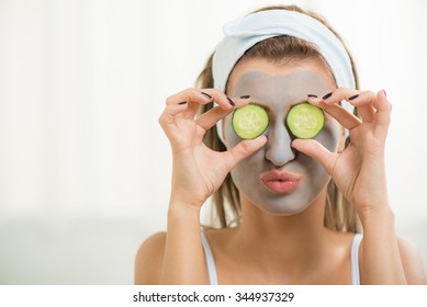 Beautiful young Woman in clay mud mask on face covering eyes with slices cucumber. 