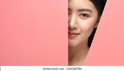 Beautiful Young Woman With Clean Fresh Skin.Asian Girl With Beautiful Brown Bright Eyes,expressive Eyebrows Looks Into The Hole Of Pink Colored Paper.Fashion,cosmetics,beauty,beauty Salon,make-up.