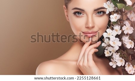 Beautiful young woman with clean fresh skin touching her face in flowers  . Girl facial  treatment   . Cosmetology , beauty  and spa . Female  model, care concept 