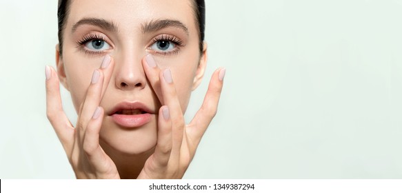 Beautiful young woman with clean perfect skin. Portrait of beauty model with natural nude make up and and hand with manicure touching face. Spa, skincare and wellness. Close up, background, copyspace.