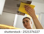 Beautiful young woman cleaning kitchen hood with napkin at home, selective focus