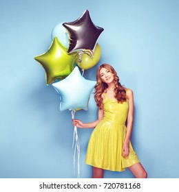 Beautiful Young Woman With Colorful Balloons On A Blue Background. Birthday And Party. Girl In Green Dress At The Festival