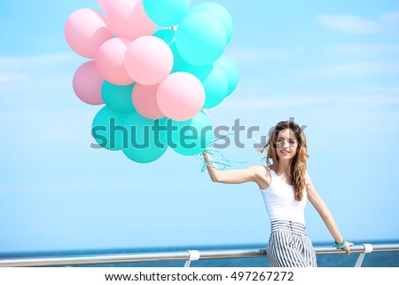 Beautiful young woman with colorful balloons on sea front