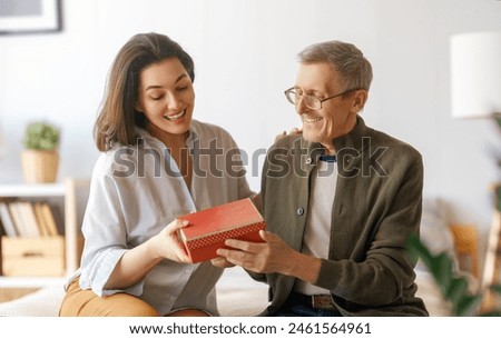 Beautiful young woman congratulating father and giving to him a gift.  