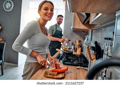 Beautiful Young Woman Cooking In The Kitchen, Chopping Peppers And Mushrooms Smiling And Looking At The Camera. Family Morning.