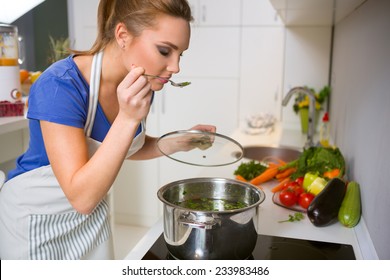 Beautiful Young Woman Cooking And Testing The Food In The Kitchen