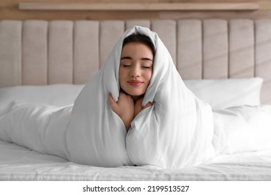 Beautiful young woman covered with warm blanket on bed at home