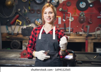 Beautiful Young Woman Craftsman Engineer Stands In Apron On Background Of Tools For Crafting. Concept Small Business In Garage Industrial Room.