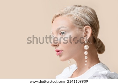 Beautiful young woman with creative makeup and stylish earrings on light background