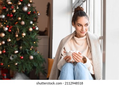 Beautiful Young Woman With Cup Of Hot Chocolate Near Window At Home On Christmas Eve